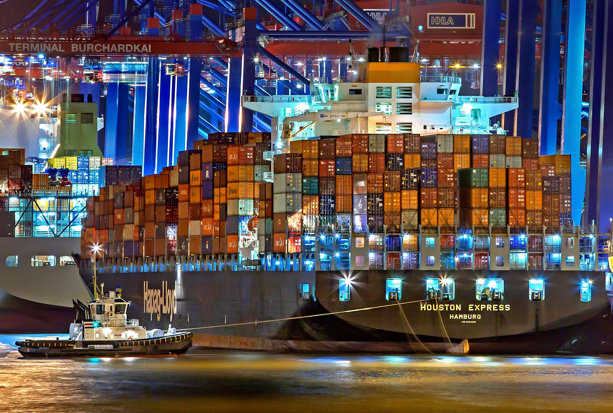 Large container ship docked at a brightly lit cargo terminal at night